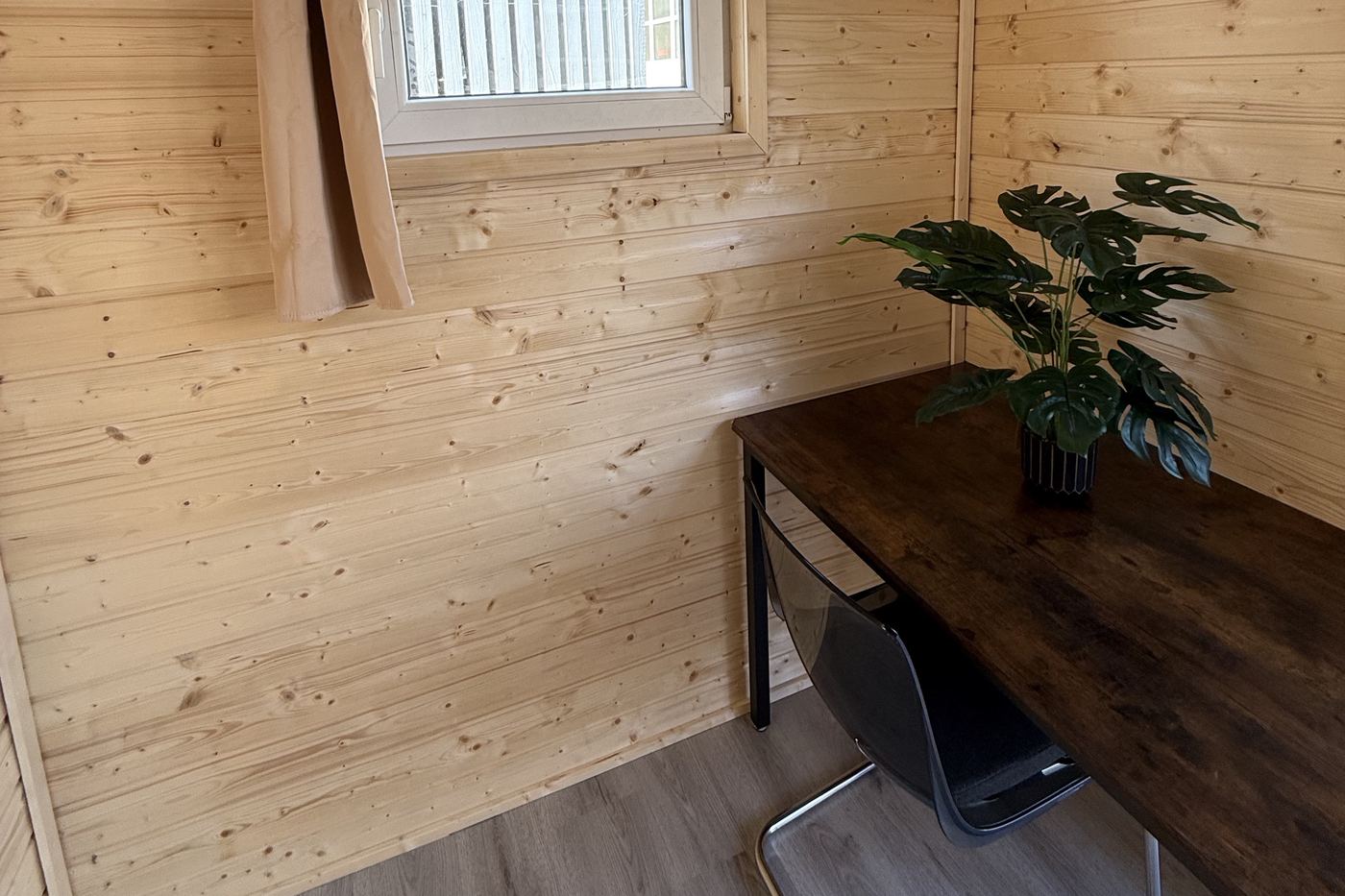 Schreibtisch mit Stuhl und Pflanze in einem Sleep Cube mit Holzwänden und Fenster.