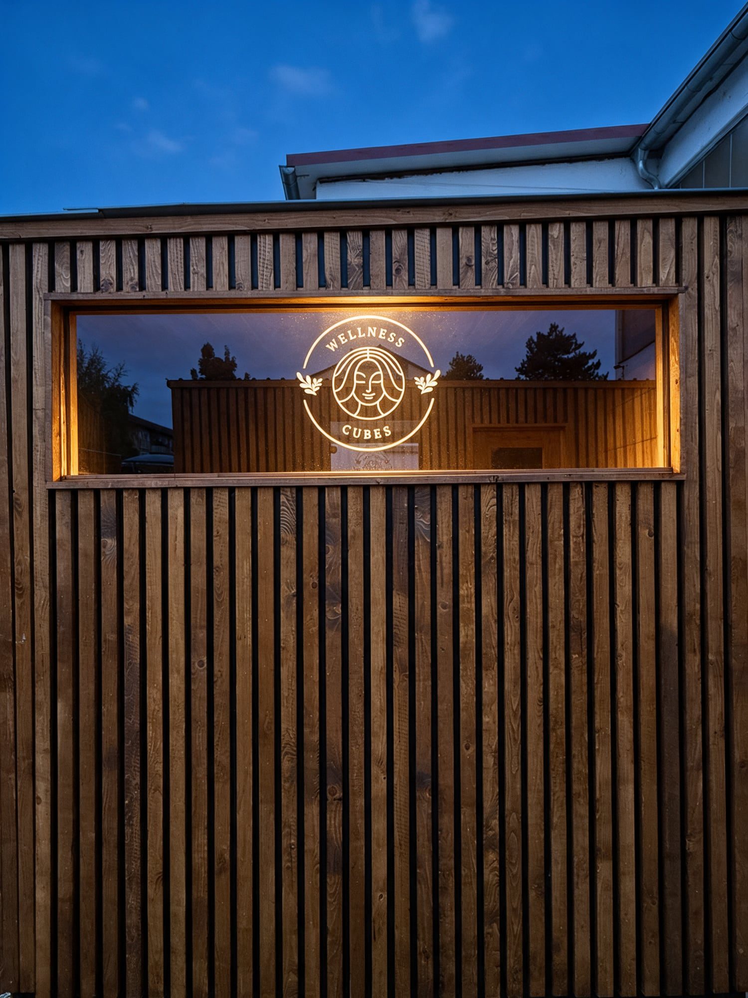 Visualisierung: Fassade des Wellness Cube mit eingeätzter Wortmarke im Fenster zur blauen Stunde.