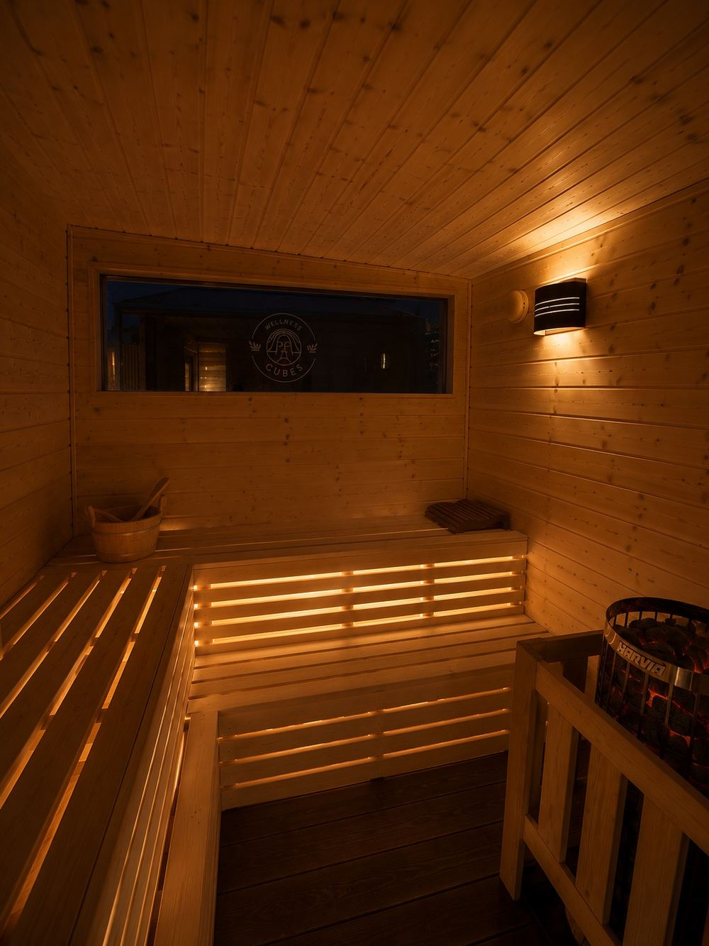 Saunaraum im Wellness Cube mit indirekt beleuchteten Bänken, Ofen und Fenster.