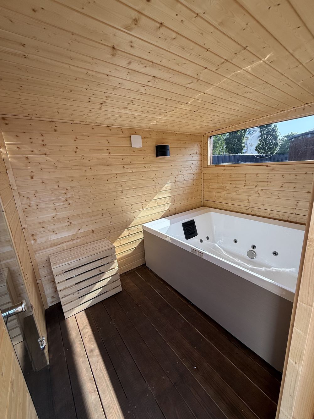 Whirlpool für zwei Personen im Vorraum eines Wellness Cube, Holzverkleidung, Fenster zum Garten.