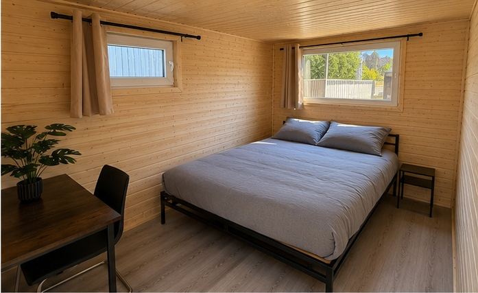Innenraum eines Sleep Cube mit Doppelbett, Schreibtisch und zwei Fenstern.